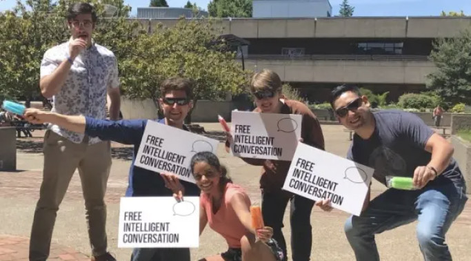 A group outdoors holds signs reading Free Intelligent Conversation.